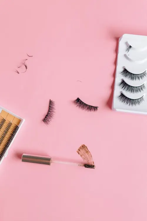 Lash strips, lash trays and a brow gel brush laid out on pink